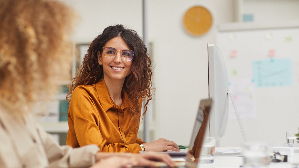 kvinna tittar leende på kollega vid arbetsbord