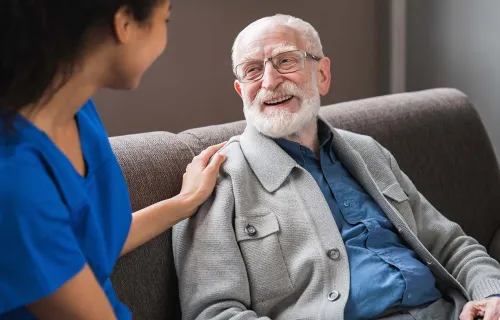 Healthcare professional placing a comforting hand on elderly patient's shoulder