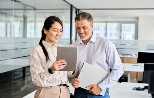 Two people standing and smiling while reviewing a tablet
