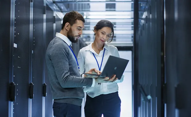 two professionals in a server room looking at a laptop