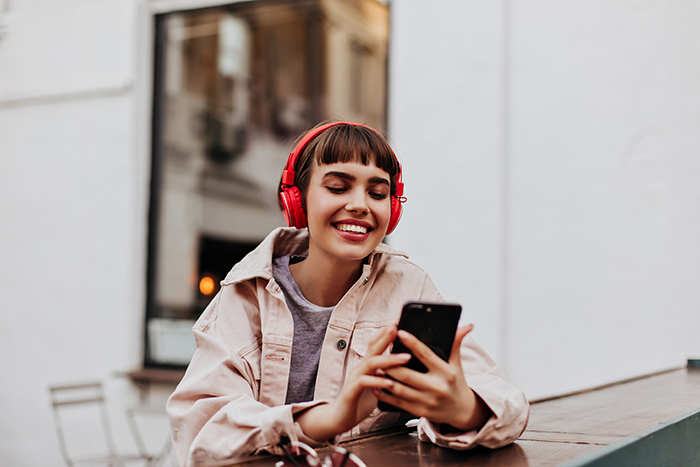 woman with headphones on smiling while looking down at her cellphone 