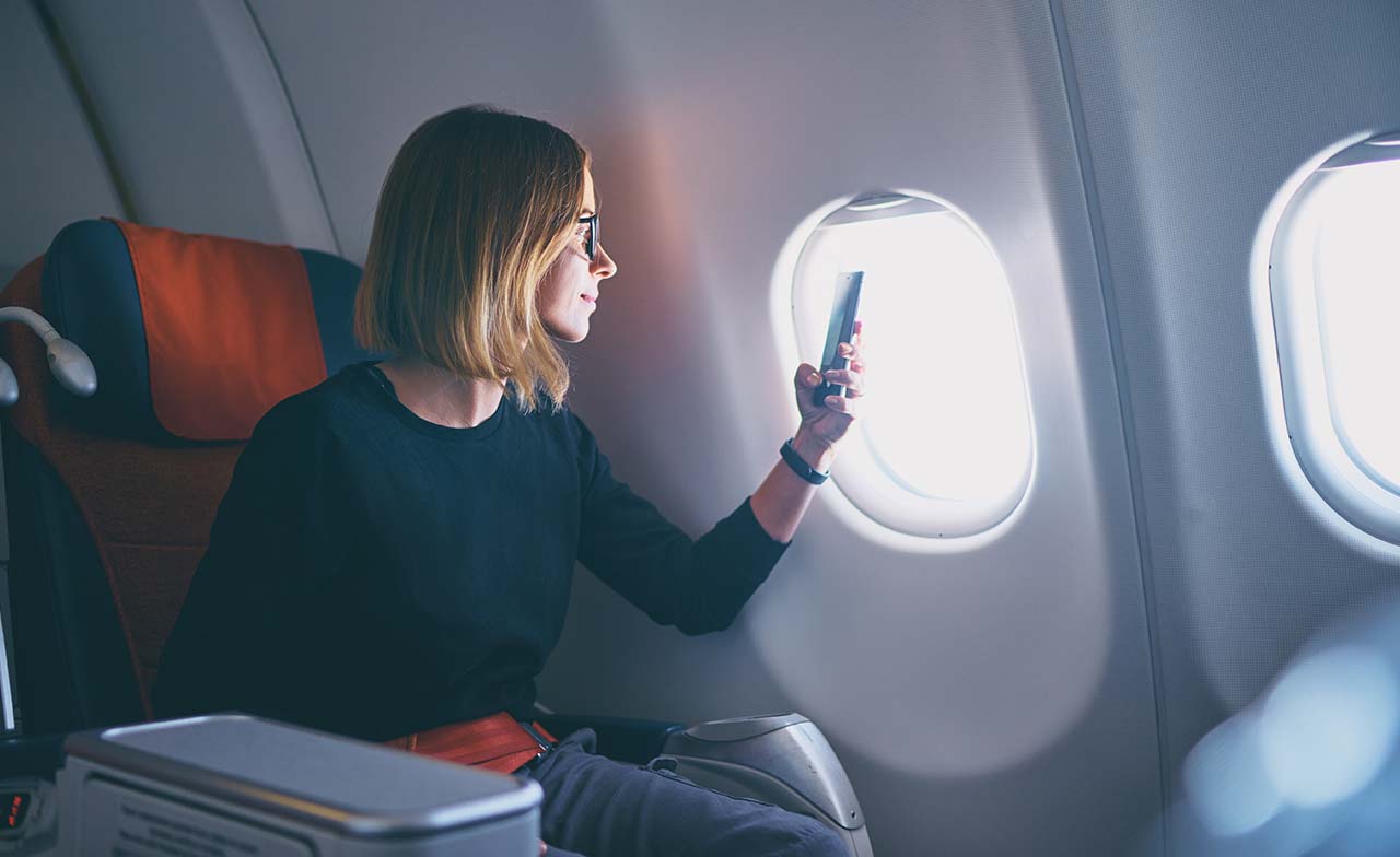 Geschäftsfrau, die im Flugzeug sitzend ein Foto mit ihrem Smartphone macht