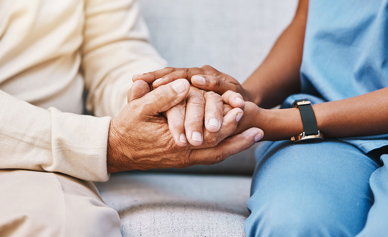 A close up of two people holding hands En närbild av två personer som håller varandra i händerna. En äldre persons händer vilar i händerna på en yngre person, vilket förmedlar en känsla av stöd och omsorg.