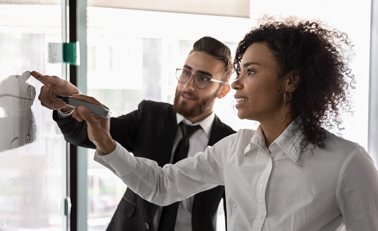 Zwei Berater diskutieren ihre Strategie an einem Whiteboard Zwei Berater diskutieren ihre Strategie an einem Whiteboard