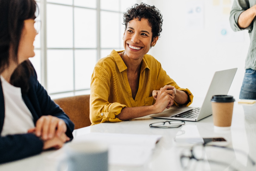 Consultant sitting in front of laptop talking to a colleague