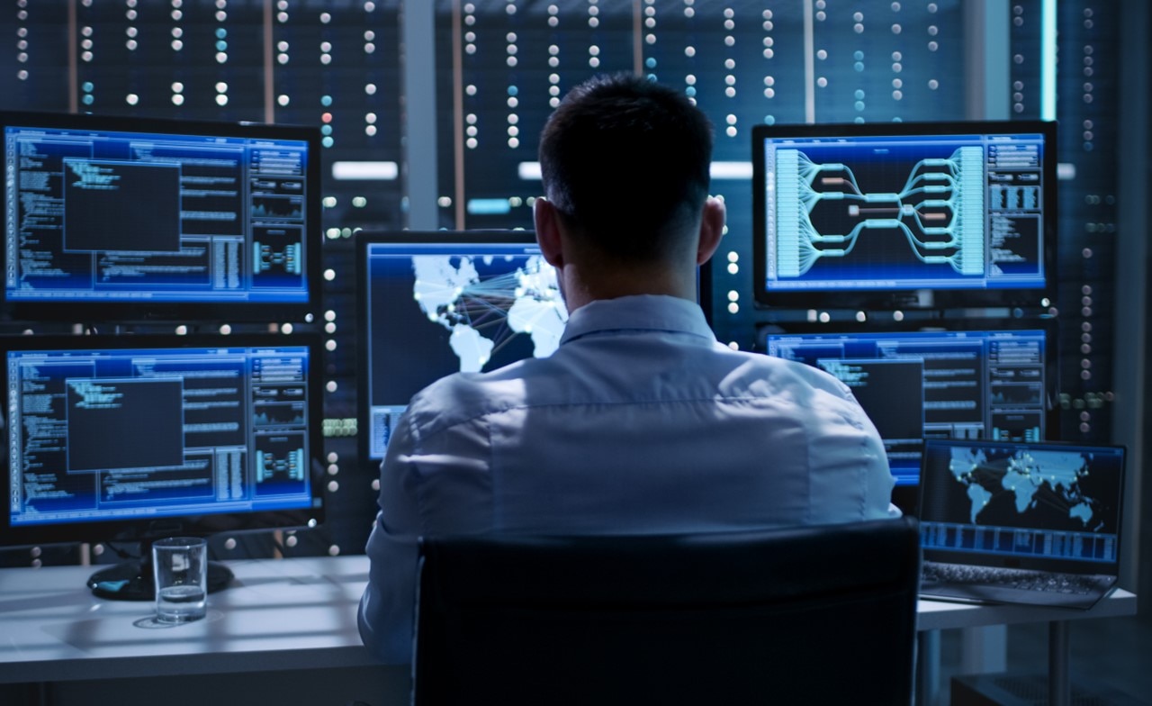 Male cyber security professional in a SOC environment looking at multiple computer screens showing organisational information