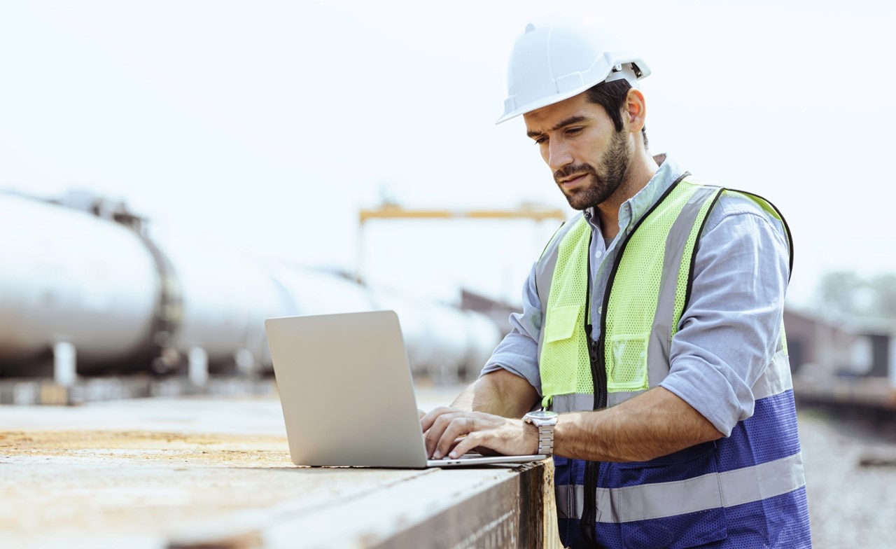 Field worker wearing a hardhat working on a computer