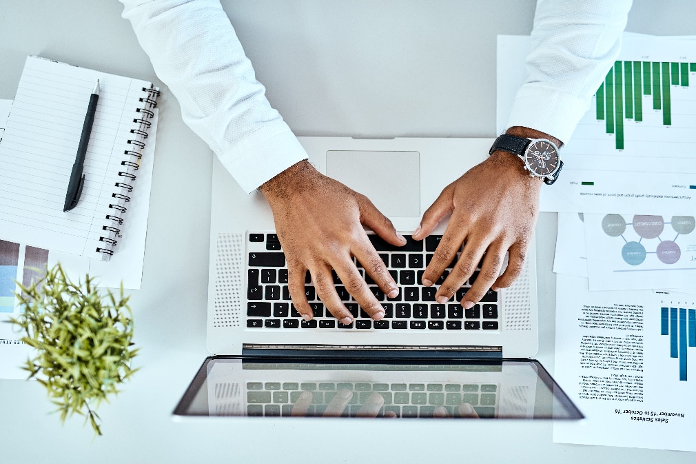 Above view of hands typing on laptop surrounded by documents