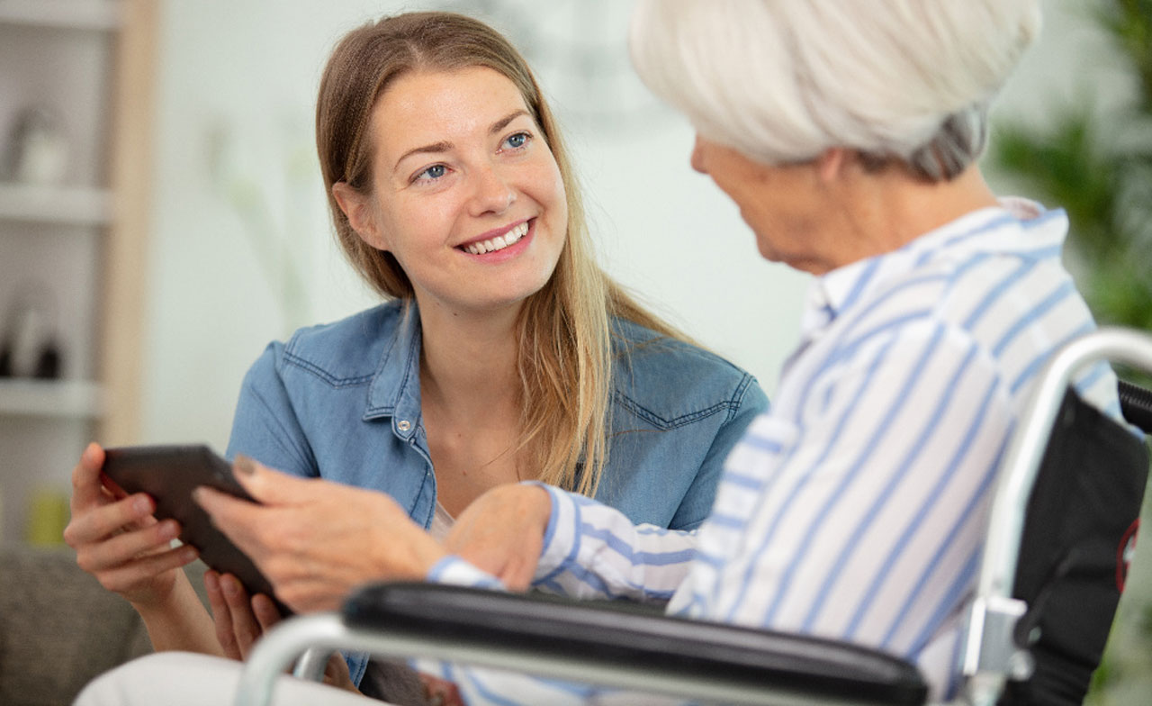 Healthcare working showing a tablet to woman in wheelchair