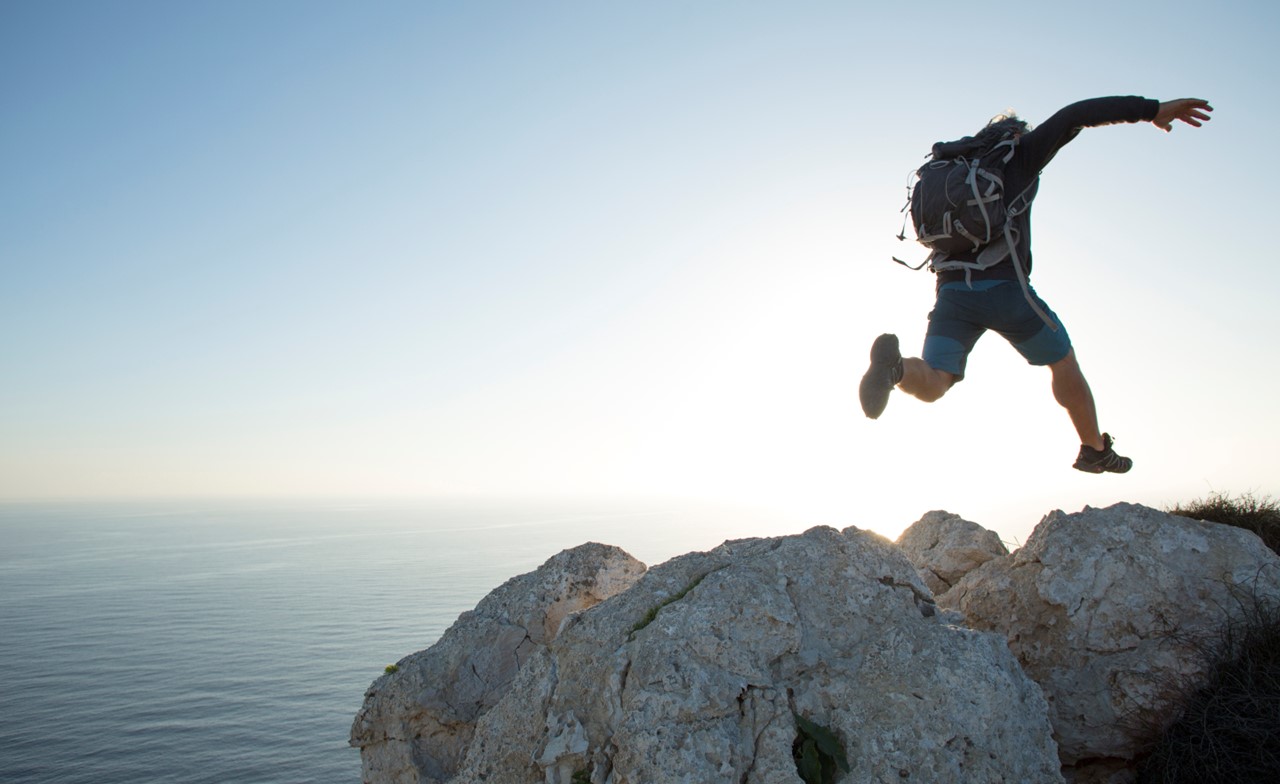 A hiker jumping over rocks along the coast