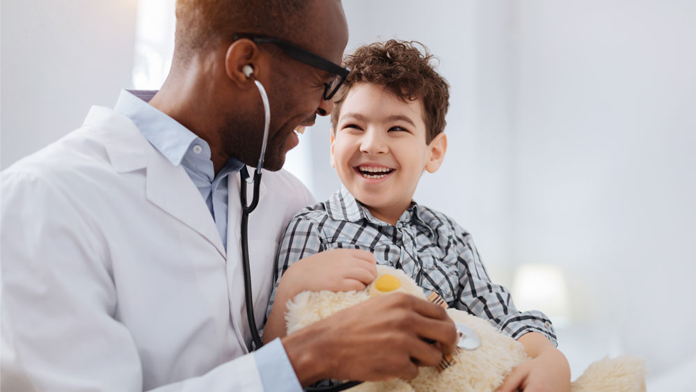 Arzt hält ein Kind auf seinem Arm und beide lachen 