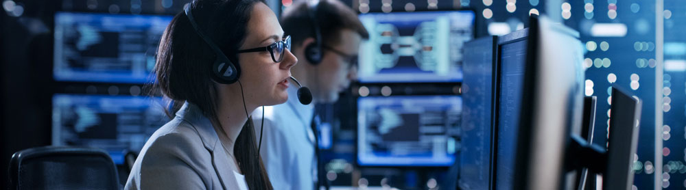 Two people with headsets sit in a control centre