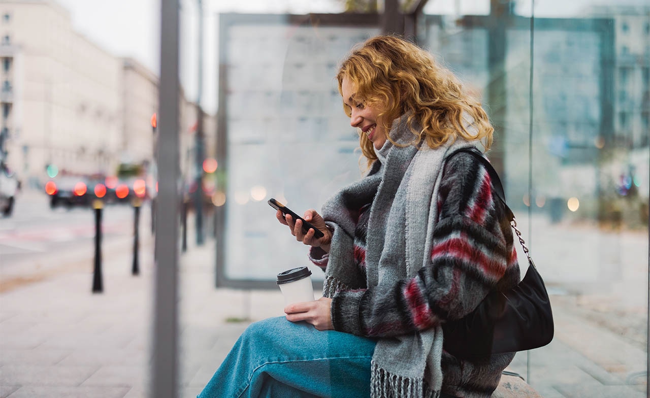 young woman waiting for public transport and looking at her phone