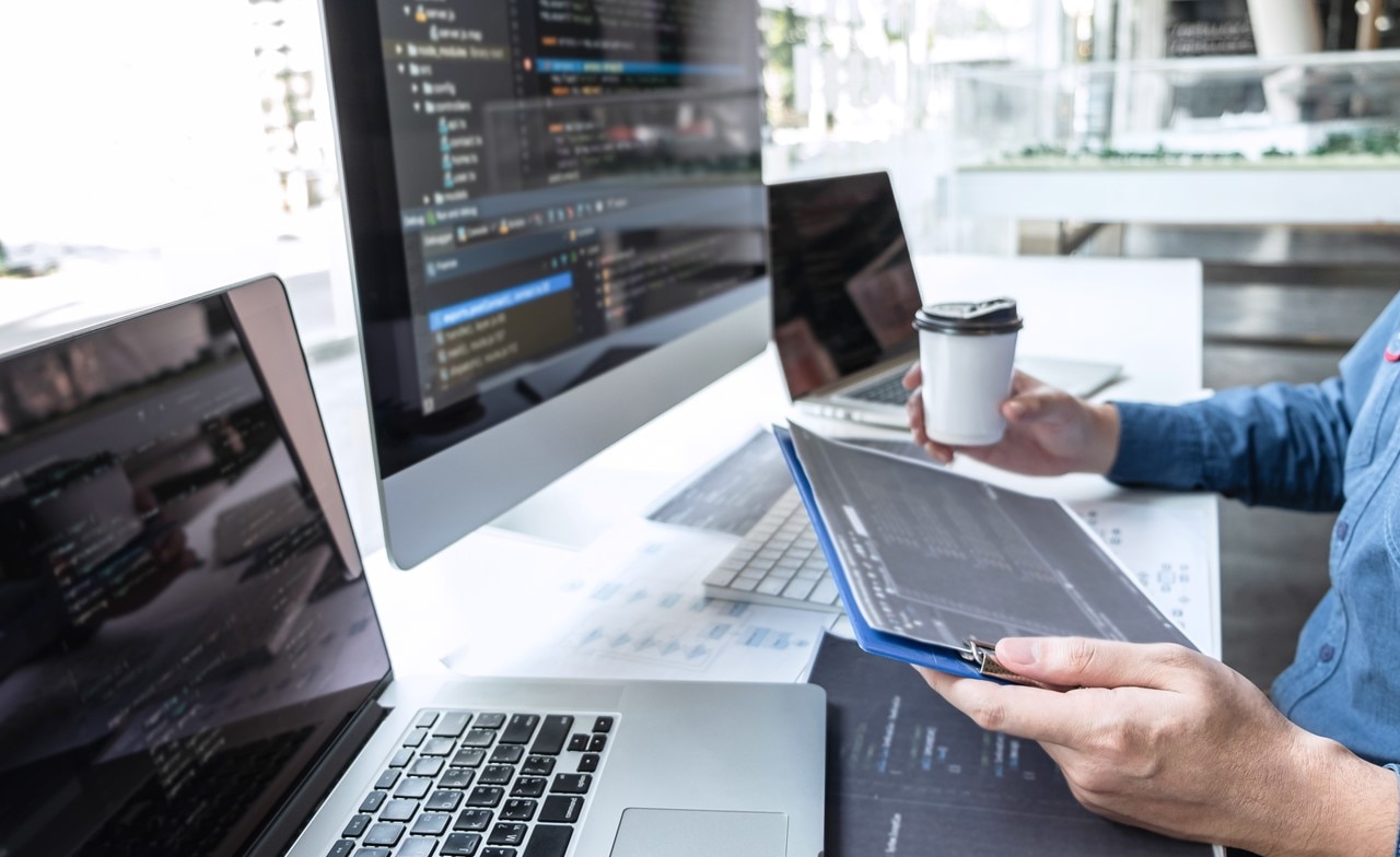 A person holding a cup of coffee and documents while looking at a computer