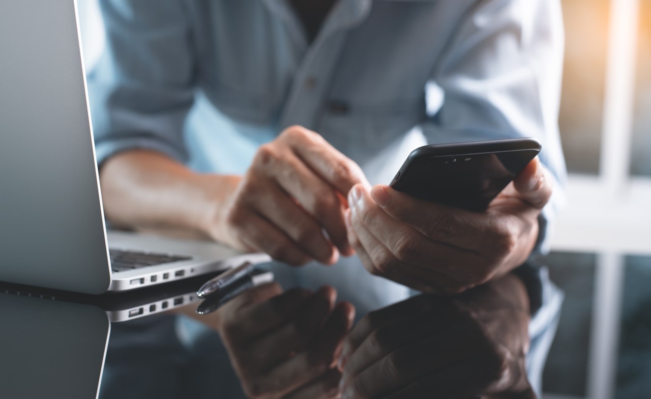 Person in front of a laptop looking at a mobile phone