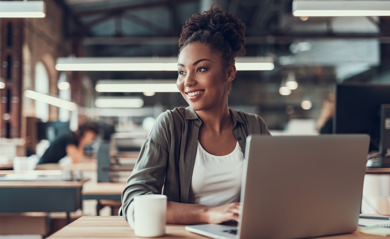 A smiling person sitting at a table with a computer