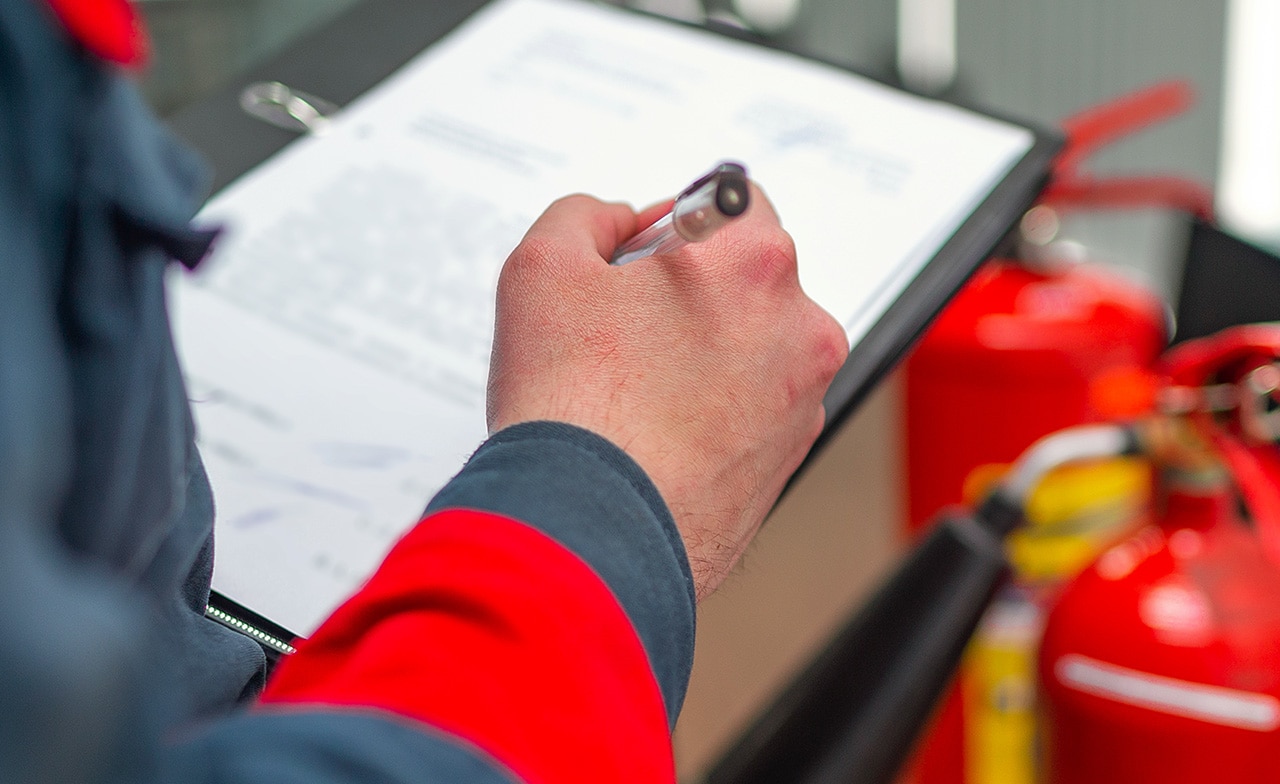 Person with clipboard standing in front of two fire extinguishers