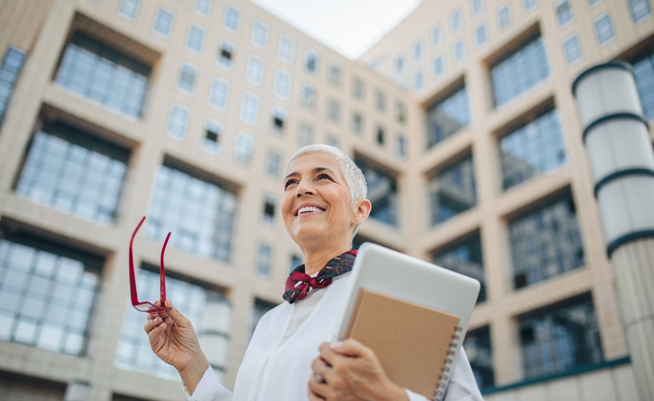 A smiling person holding a notebook and glasses