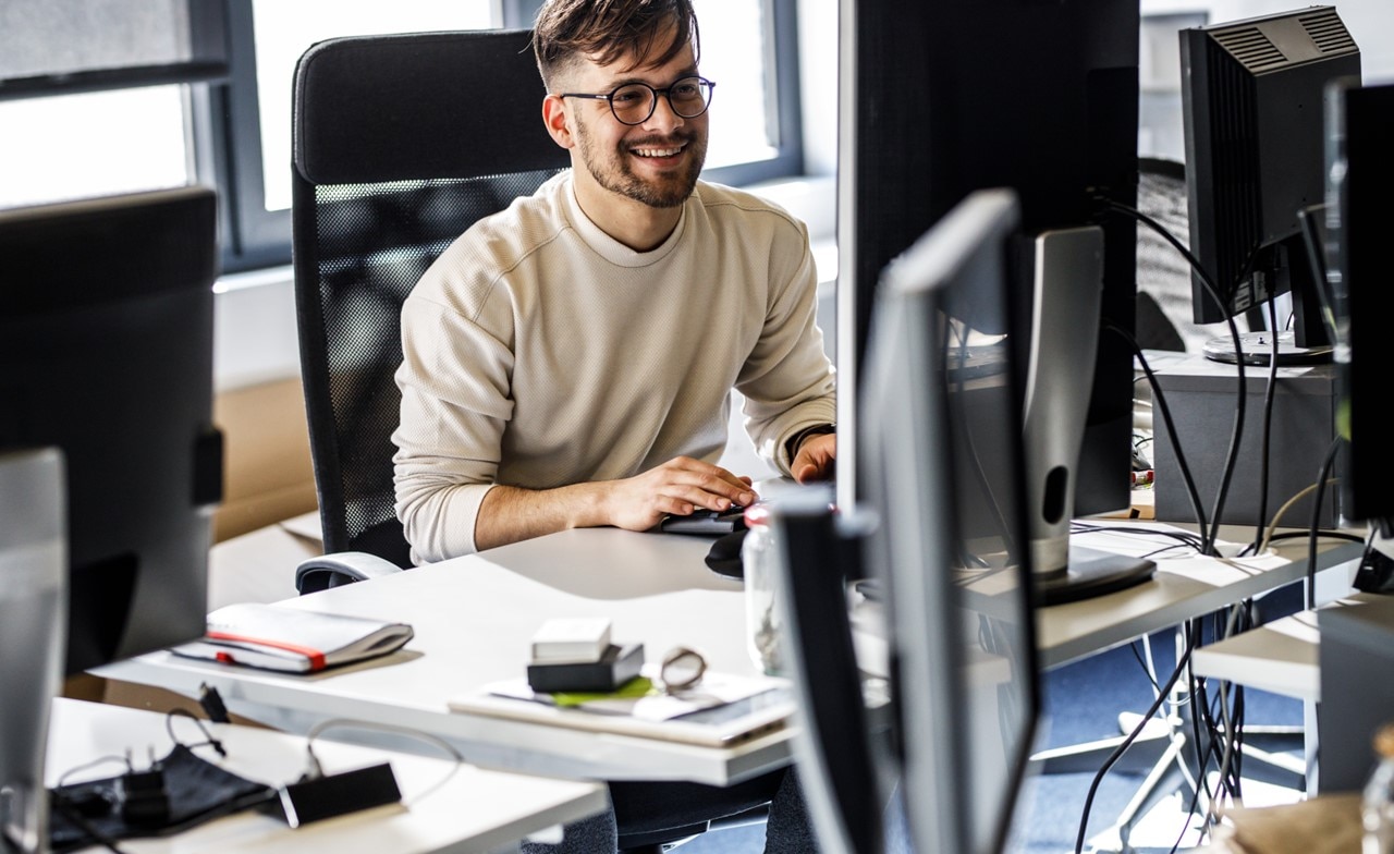 A smiling person sitting at a computer desk