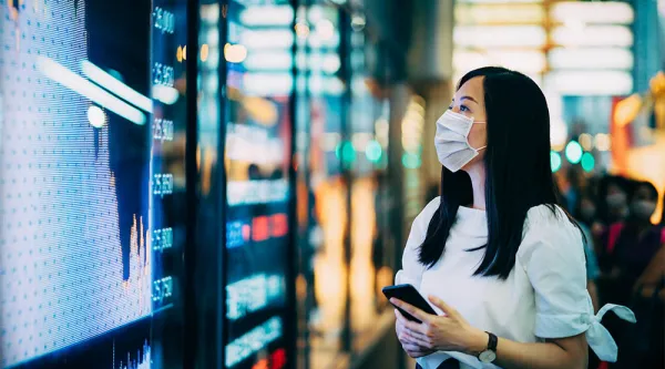 woman in a medical facemask looking at figures ona digital display board