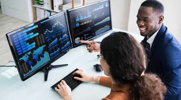 two consultants looksing at data together on two monitors