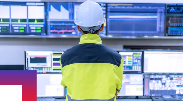 A utilities worker in hardhat looking at data in a computer control center