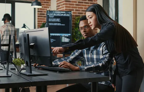 Two programers holding laptop with coding interface walking towards desk and sitting down…