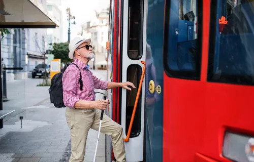 En blind man med en vit käpp kliver på en röd buss