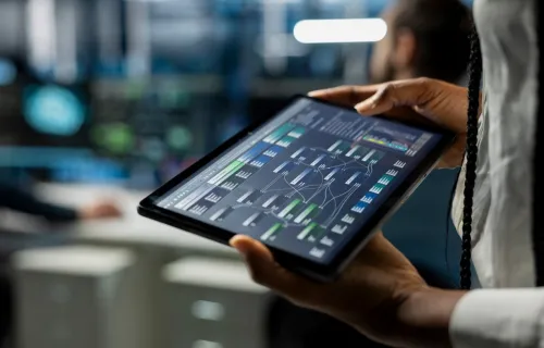Person holding a tablet displaying a digital dashboard in a modern technology workspace.