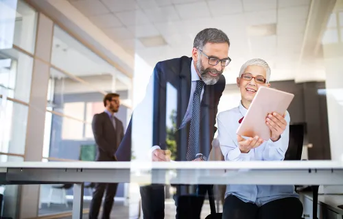 Zwei Kollegen in einer Bank freuen sich über den erfolgreichen KI-gestützten Onboarding-Prozess auf einem Tablet