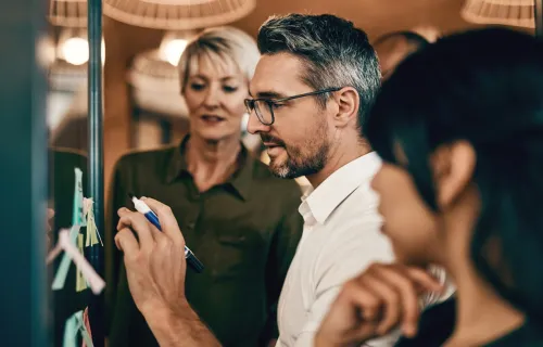 Team nutzt New-Learning-Methoden und arbeitet gemeinsam an einem Whiteboard, um Veränderungen in der Verwaltung zu planen.