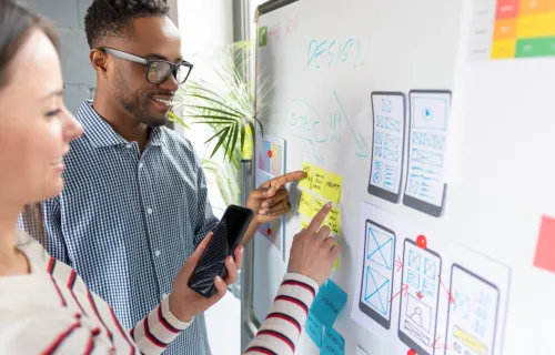 Zwei Personen stehen vor einem Whiteboard und haben PostITs in der Hand