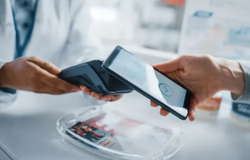 Ein Apotheker und ein Kunde verwenden ein Smartphone mit kontaktlosem Bezahlterminal, um verschreibungspflichtige Medikamente zu kaufen