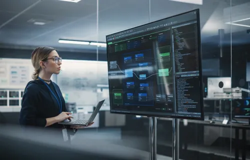 Cyber consultant on laptop looks at data on big screen