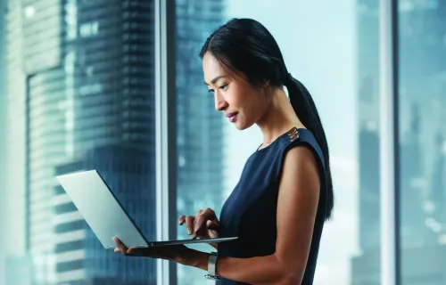 Female professional standing with laptop near office window