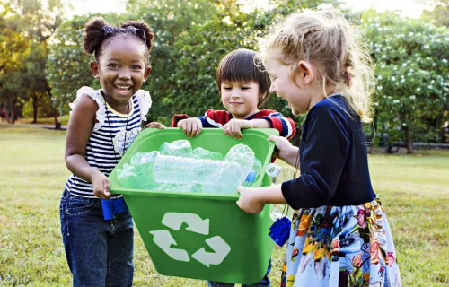 Infant school aged children carry a recycling bin 