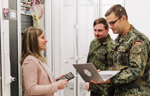 3 CGI Member stehen in einem Rechenzentrum, zwei davon tragen eine Bundeswehruniform