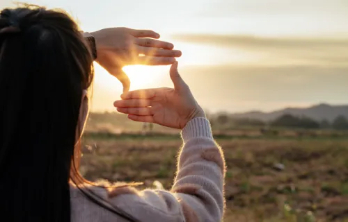mujer enmarcando el sol con sus manos