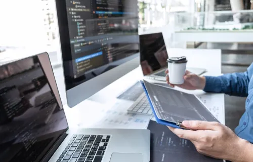 Person holding coffee and tablet at computer desk