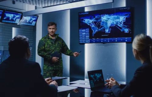 Military personnel having a meeting in front of computer screen and laptops