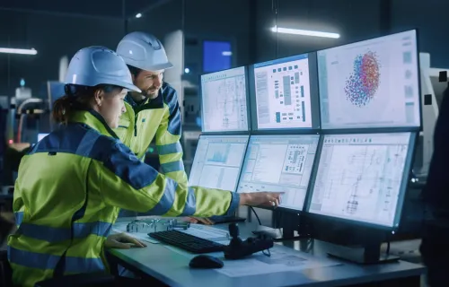 Two OT engineers examining infrastructure on multiple computer screens 