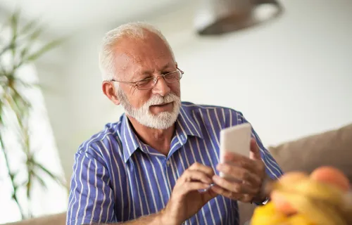 Pensionär anvander smartphone med två händer och ler