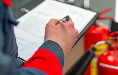 Person with clipboard standing in front of two fire extinguishers