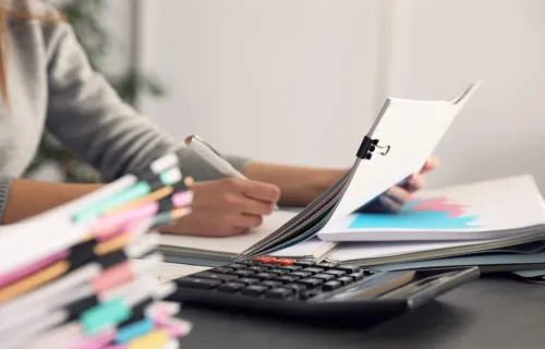 person checking paperwork and commissions figures at a desk with a calculator 