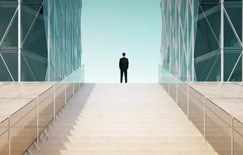 Man steht zwischen zwei hohen Glasgebäuden und vor ihm eine lange Treppe