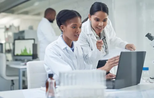 Two professionals in lab coats looking at a computer