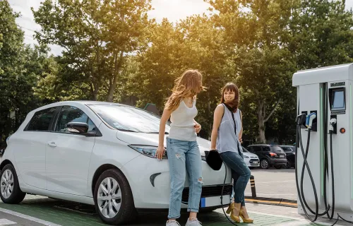 Two young women chatting while standing next to a charging EV