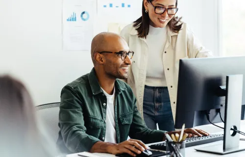 Zwei Personen arbeiten im Büro an KI-gestützter Softwareentwicklung am Computer.