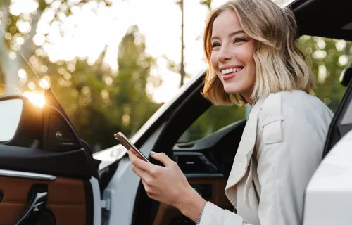 Junge Frau steigt mit einem Handy in der Hand aus einem Auto aus.