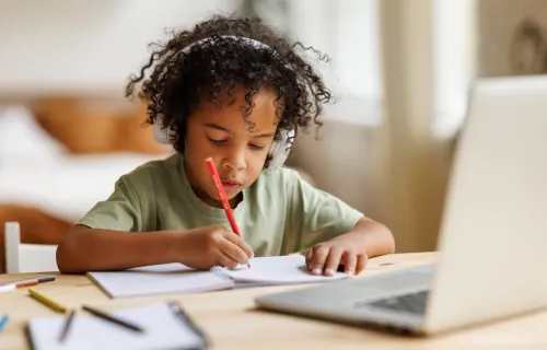 A young child wearing headphones writing on a notepad